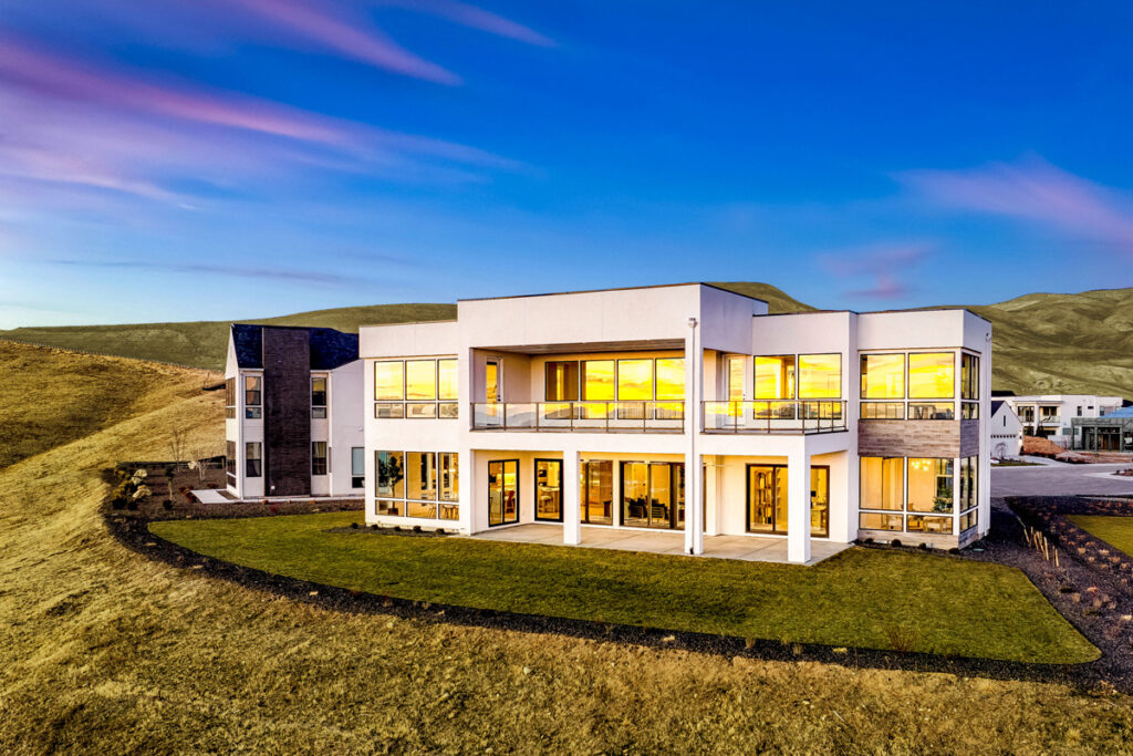 Back of a beautiful modern home with the lights on in the evening.