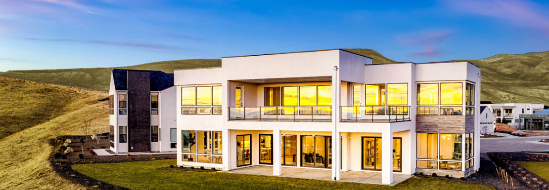Back of a beautiful modern home with the lights on in the evening.